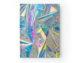 Op de afbeelding: Een rechthoekig notitieboek met een omslag met een holografisch, iriserend ontwerp. De omslag heeft een gekreukeld, reflecterend uiterlijk met tinten blauw, paars en geel. Het notitieboek staat tegen een witte achtergrond.