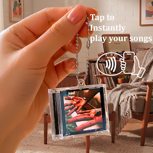 May include: A square, clear acrylic keychain featuring a miniature album cover insert with a photograph of hands. The keychain includes a silver-toned metal ball chain and displays the text Tap to Instantly play your songs with a wireless signal icon.