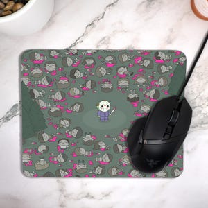 May include: A rectangular mousepad with a cartoon illustration. The design features a character in a hockey mask holding a bloody knife, surrounded by cartoon figures lying on the ground with pink blood. The background is a muted green with two green trees.