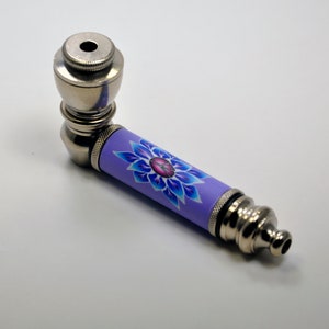 May include: A silver metal pipe with a purple and blue floral design. The pipe has a bowl at one end and a mouthpiece at the other.