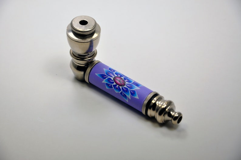 May include: A silver metal pipe with a purple and blue floral design. The pipe has a bowl at one end and a mouthpiece at the other.