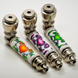 May include: Three metal pipes with white painted designs featuring colorful hearts and flowers. The pipes are silver with a shiny finish.