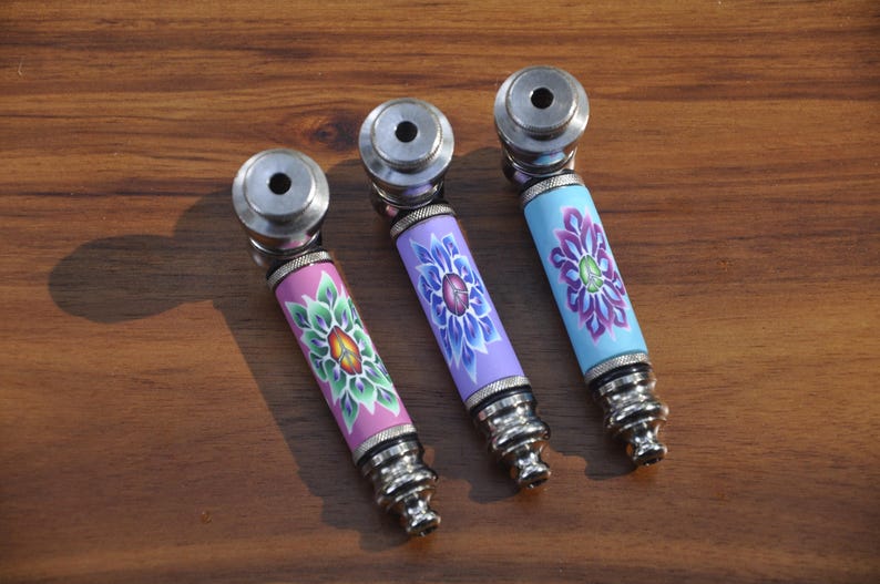 May include: Three metal smoking pipes with colourful floral designs. The pipes are silver with a pink, purple, and blue floral pattern.