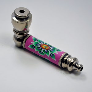 May include: A silver metal smoking pipe with a pink and green floral design. The pipe has a bowl at one end and a mouthpiece at the other.