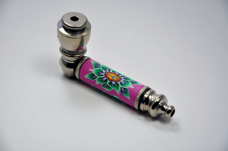 May include: A silver metal smoking pipe with a pink and green floral design. The pipe has a bowl at one end and a mouthpiece at the other.