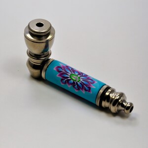 May include: A silver metal smoking pipe with a blue and purple floral design on the stem.