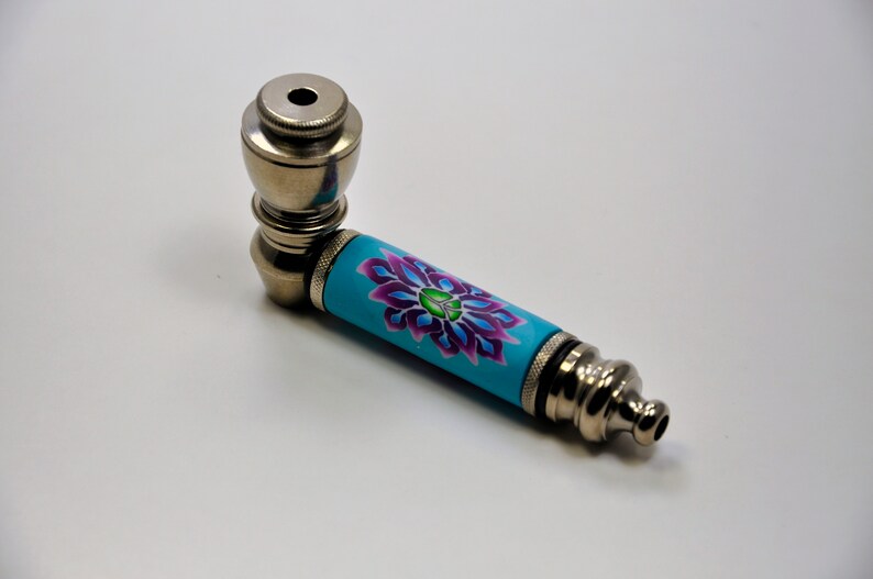 May include: A silver metal smoking pipe with a blue and purple floral design on the stem.