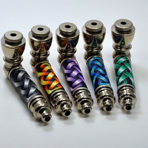Puede incluir: Cinco pipas para fumar de metal con diseños de nudos celtas de diferentes colores. Las pipas son plateadas con un acabado brillante.