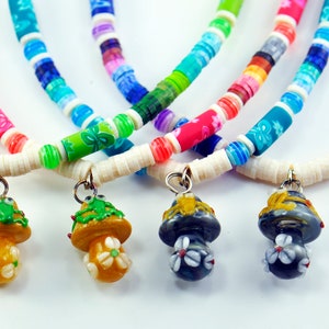 May include: Four colorful beaded necklaces with mushroom charms. Each necklace features a different color scheme with white beads and a variety of colorful beads. The mushroom charms are made of ceramic and have different colors and designs.