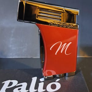 May include: A Palio Pro lighter with a red body and a gold-colored top. The lighter has the letter "M" in white script on the red body. The Palio Pro logo is visible on the box.