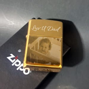 May include: Gold lighter with a photo of a baby and the inscription "Luv U Dad" engraved on the front.