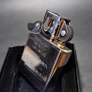 May include: A chrome-plated Zippo lighter, with the text "FOR BEST RESULTS USE ZIPPO FLINTS AND FLUID" and "ZIPPO MADE IN U.S.A." The lighter is in a black box. The lighter is a classic, durable design.