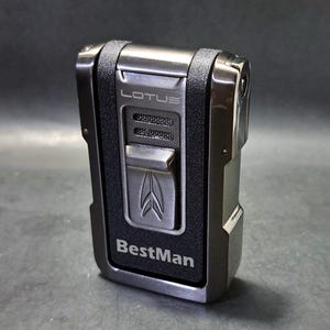 May include: A black and silver Lotus BestMan lighter. The lighter has a textured black grip and a silver metal frame. The word "LOTUS" is above the ignition button, and the word "BestMan" is below it.