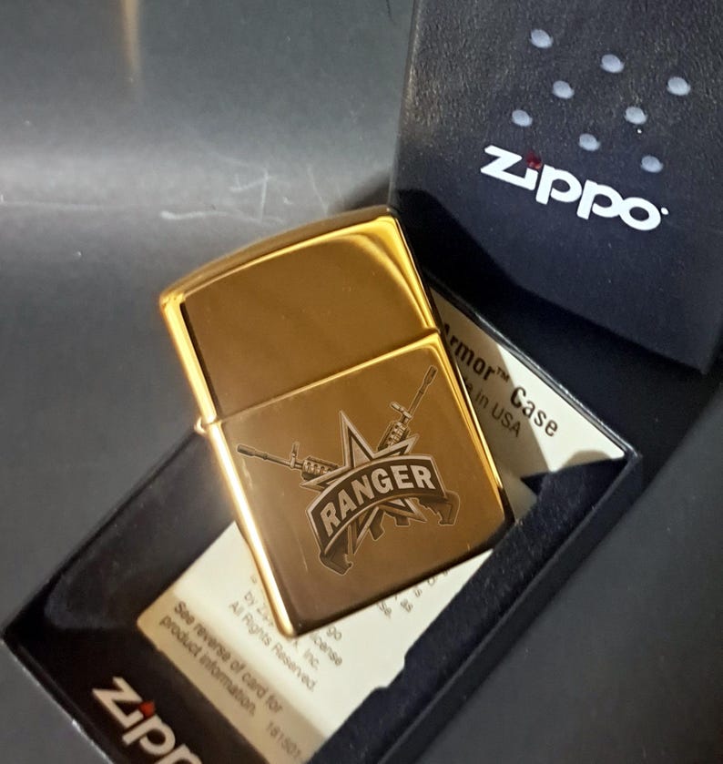 May include: Gold Zippo lighter with an engraved design of a star, two rifles, and the word "RANGER". The lighter is in a black box with the Zippo logo.