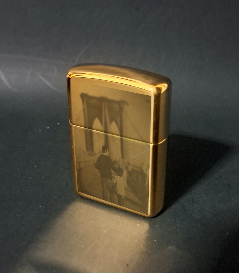May include: A gold-colored lighter with an engraved image of the Brooklyn Bridge and a couple walking across it.