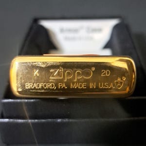 May include: Gold-colored Zippo lighter with the text "K Zippo 20 Bradford, PA. Made in U.S.A." on the bottom.