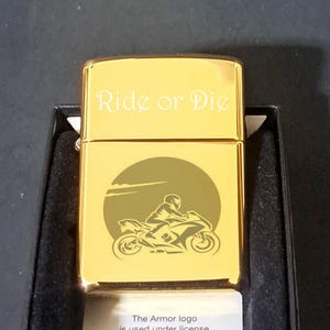 May include: Gold-colored lighter with an engraved image of a motorcycle rider and the words "Ride or Die".