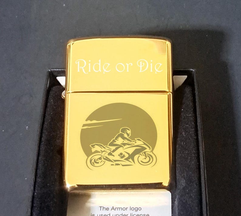 May include: Gold-colored lighter with an engraved image of a motorcycle rider and the words "Ride or Die".