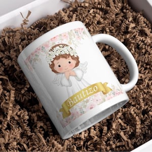 Puede incluir: Taza de cerámica blanca con un diseño floral y un ángel de dibujos animados con un halo. La taza tiene la palabra "Bautizo" escrita en letras doradas.