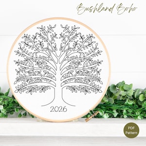Op de afbeelding: Een zwart-wit kruissteekpatroon van een boom in een houten borduurring. De boom heeft veel bladeren en takken, met het jaartal "2026" aan de basis. De woorden "Bushland Boho" staan ​​bovenaan in cursief.