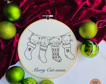 May include: A white embroidery hoop with a black and white illustration of four cats wearing Christmas stockings. The text "Merry Cat-mass" is written below the cats. The hoop is surrounded by green Christmas ornaments.