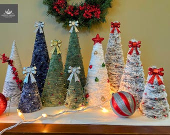 May include: A collection of decorative Christmas trees in various sizes and colors. The trees are adorned with bows, stars, and ornaments. A red and silver striped ball and a string of lights add to the festive display.