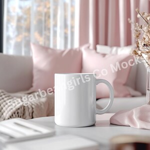 May include: White ceramic mug on a white table with a pink throw blanket and pillows in the background.
