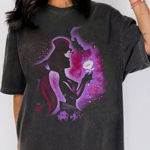 Puede incluir: Una camiseta negra con un estampado gr&aacute;fico descolorido en morado y blanco de una pareja sosteniendo una flor. El gr&aacute;fico es una silueta de un hombre y una mujer con una flor blanca en el centro.