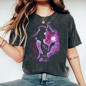 Puede incluir: Una camiseta gris oscuro con una silueta morada y blanca de una pareja sosteniendo una flor. La silueta se coloca sobre un fondo de galaxia morada y blanca. La camiseta tiene un aspecto desgastado.