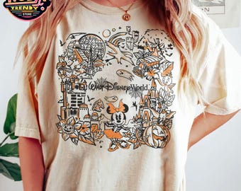 May include: Cream-colored t-shirt featuring a detailed orange and black graphic of Disney World attractions, including a castle, Minnie Mouse, and pumpkins. The text "Walt Disney World" is also visible. The shirt has a crew neck and short sleeves.