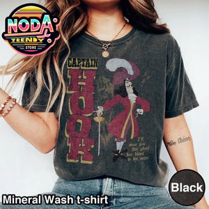 May include: Black mineral wash t-shirt featuring a Captain Hook graphic. The design includes the text "CAPTAIN HOOK" in burgundy, a cartoon image of Captain Hook, and the quote "I'll show you this ghost has blood in his veins."