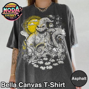 May include: Dark gray Bella Canvas T-shirt featuring a graphic of a character with a large grin, a full moon, and other spooky elements. The shirt has the text "Bella Canvas T-Shirt" at the bottom.