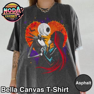 以下が含まれることがあります： アスファルトカラーのBella Canvas Tシャツ。映画「ナイトメアー・ビフォア・クリスマス」のジャック・スケリントンとサリーのグラフィックが特徴。背景は、コウモリとクモの巣のデザインが施された、ハート型のオレンジと紫です。