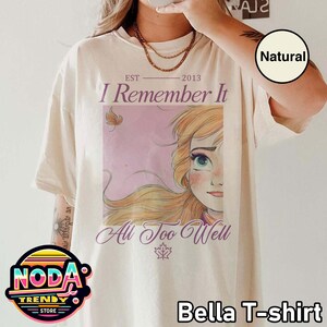 Puede incluir: Camiseta Bella color crema con un gr&aacute;fico de un personaje de dibujos animados y el texto "I Remember It All Too Well". La camiseta tambi&eacute;n tiene el texto "EST 2013" impreso encima del gr&aacute;fico.