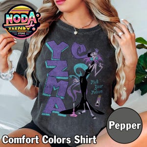 Pu&ograve; includere: Maglietta grigio scuro Comfort Colors con una grafica di Yzma da Le follie dell'imperatore. La maglietta presenta la parola "Yzma" in lettere viola e la frase "Pick Your Poison".