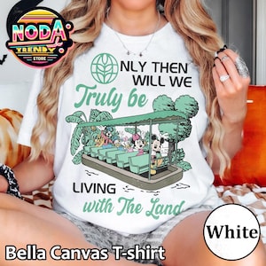 Könnte beinhalten: Weißes Bella Canvas T-Shirt mit einer grün-schwarzen Grafik eines Bootes mit Disney-Figuren und dem Text "ONLY THEN WILL WE Truly be LIVING with The Land". Das T-Shirt hat einen Rundhalsausschnitt.