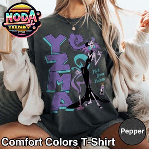 Pu&ograve; includere: T-shirt Comfort Colors grigio scuro con il nome "Yzma" in lettere viola. La maglietta presenta una grafica di un personaggio dei cartoni animati e il testo "Pick Your Poison". La parte inferiore della maglietta riporta la scritta "Comfort Colors T-Shirt".