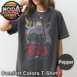 May include: Dark grey Comfort Colors T-shirt featuring a graphic of Ursula from The Little Mermaid. The design includes Ursula, a trident, and the text "URSULA". The shirt also has the text "Foor unfortunate souls."
