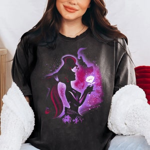 Puede incluir: Una camiseta negra con una silueta morada y blanca de una pareja bes&aacute;ndose. La silueta est&aacute; rodeada de un fondo gal&aacute;ctico morado y blanco. La mujer sostiene una flor blanca.