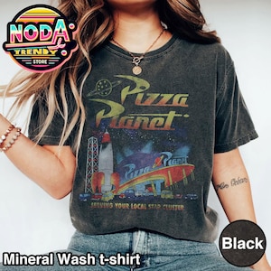 May include: Black mineral wash t-shirt featuring the Pizza Planet logo with a rocket ship and the text "SERVING YOUR LOCAL STAR CLUSTER." The shirt has a vintage, distressed look.