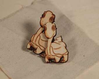 Può includere: Due figurine di tartaruga in legno, una dietro l'altra, con una finitura marrone chiaro. Le tartarughe sono rivolte nella stessa direzione, con la testa della tartaruga anteriore leggermente girata di lato.