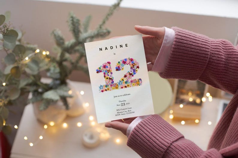 May include: A white invitation card with the name Nadine and the number 12 made of colorful flowers. The text on the card reads "Join us as we celebrate... Thursday, Nov. 23, 2023..."