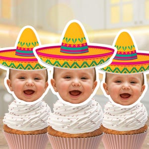 May include: Three cupcakes topped with smiling baby faces wearing colorful sombreros. The cupcakes have white frosting and are in pink cupcake liners. The sombreros are yellow with green and pink accents. The image has the text "DIGITAL FILE MADE TO ORDER".