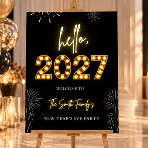 以下が含まれることがあります： 木製のイーゼルに立てられた黒い長方形の看板。hello, 2027, WELCOME TO, The Smith Family's, NEW YEAR'S EVE PARTYという文字が書かれています。2027の数字は温かみのある黄色い光で照らされており、デザインには金色の花火のグラフィックがあしらわれています。