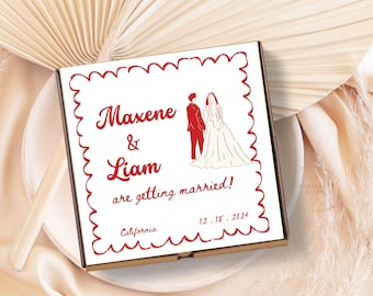 May include: A white pizza box with a red border and a red illustration of a bride and groom. The text on the box reads "Maxene & Liam are getting married! California 12.18.2024"