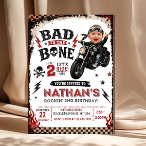 Pode incluir: Um convite de aniversário retangular com borda xadrez preta e branca, raios vermelhos e gráficos de caveiras. O texto diz Bad to the Bone, I'm 2 Let's Ride e Nathan's Rockin' 2nd Birthday, com os detalhes do evento incluídos.