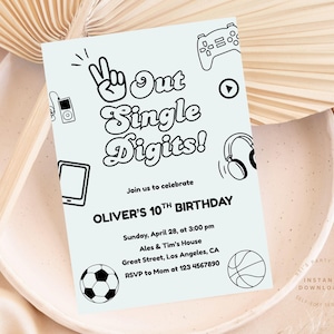 Puede incluir: Una invitación de cumpleaños azul claro con el texto "Out Single Digits!" e ilustraciones de un signo de la paz, un mando de videojuegos, auriculares y un balón de fútbol. La invitación es para el décimo cumpleaños de Oliver.