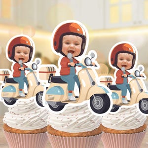 Può includere: Tre decorazioni per cupcake con un bambino su uno scooter, con casco e giacca rossi e tuta blu. Gli scooter sono color crema con dettagli blu. I cupcake hanno involucri rosa e glassa bianca.