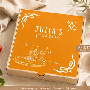 May include: A square cardboard pizza box with a bright orange lid featuring white line art of a pizza, a pitcher, and two glasses. The text reads JULIA'S pizzeria and EST 1996, accented with decorative corner swirls and star icons.