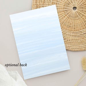 May include: A rectangular card with a light blue watercolor wash design. The text "optional back" is printed in black at the bottom left. The card is placed on a neutral surface with a woven placemat and dried floral accents.